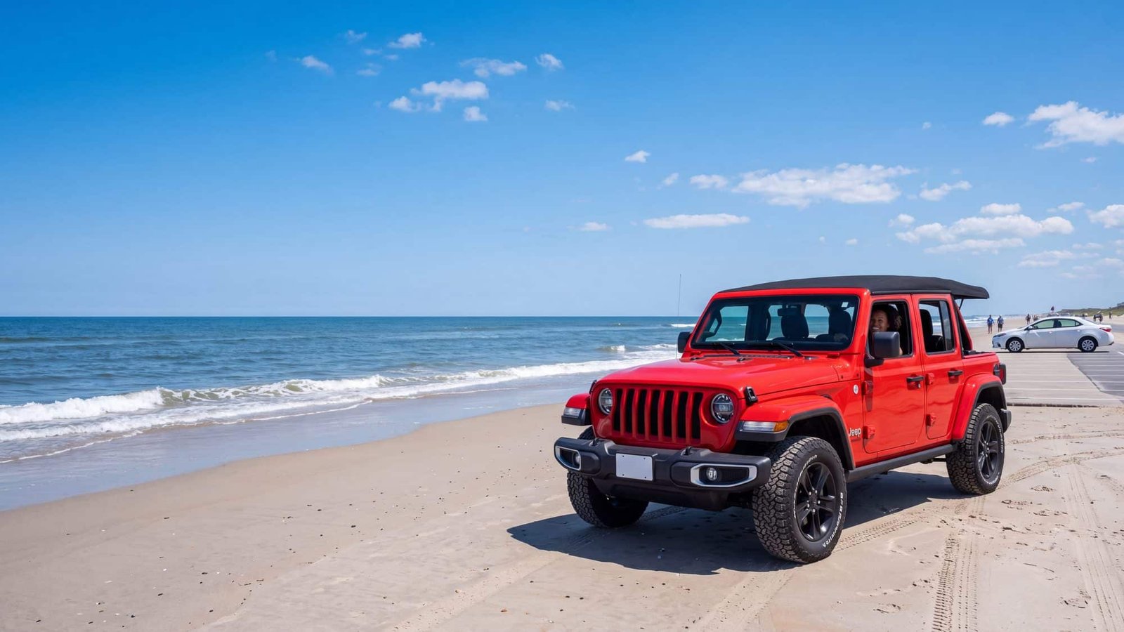 A red Jeep Wrangler JL Unlimited parked on hard sand at the surf line with its tires on the sand and a white compact rental sedan parked far back on the paved lot at the top of the beach access — Outer Banks, NC