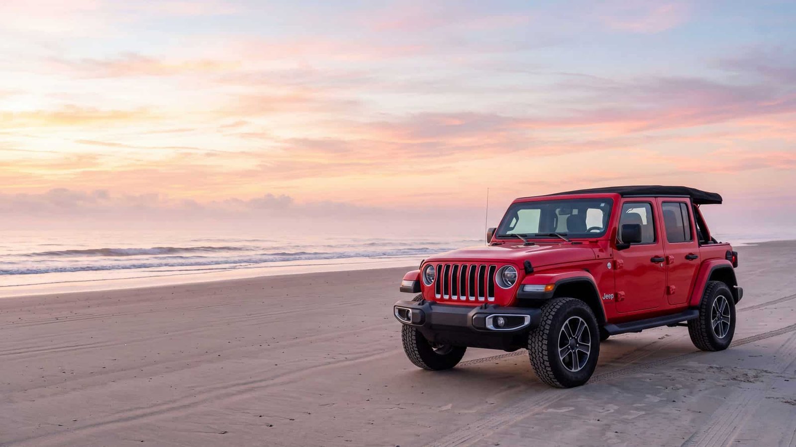 A red Jeep Wrangler JL Unlimited parked alone on a wide empty beach at dawn — Outer Banks, NC